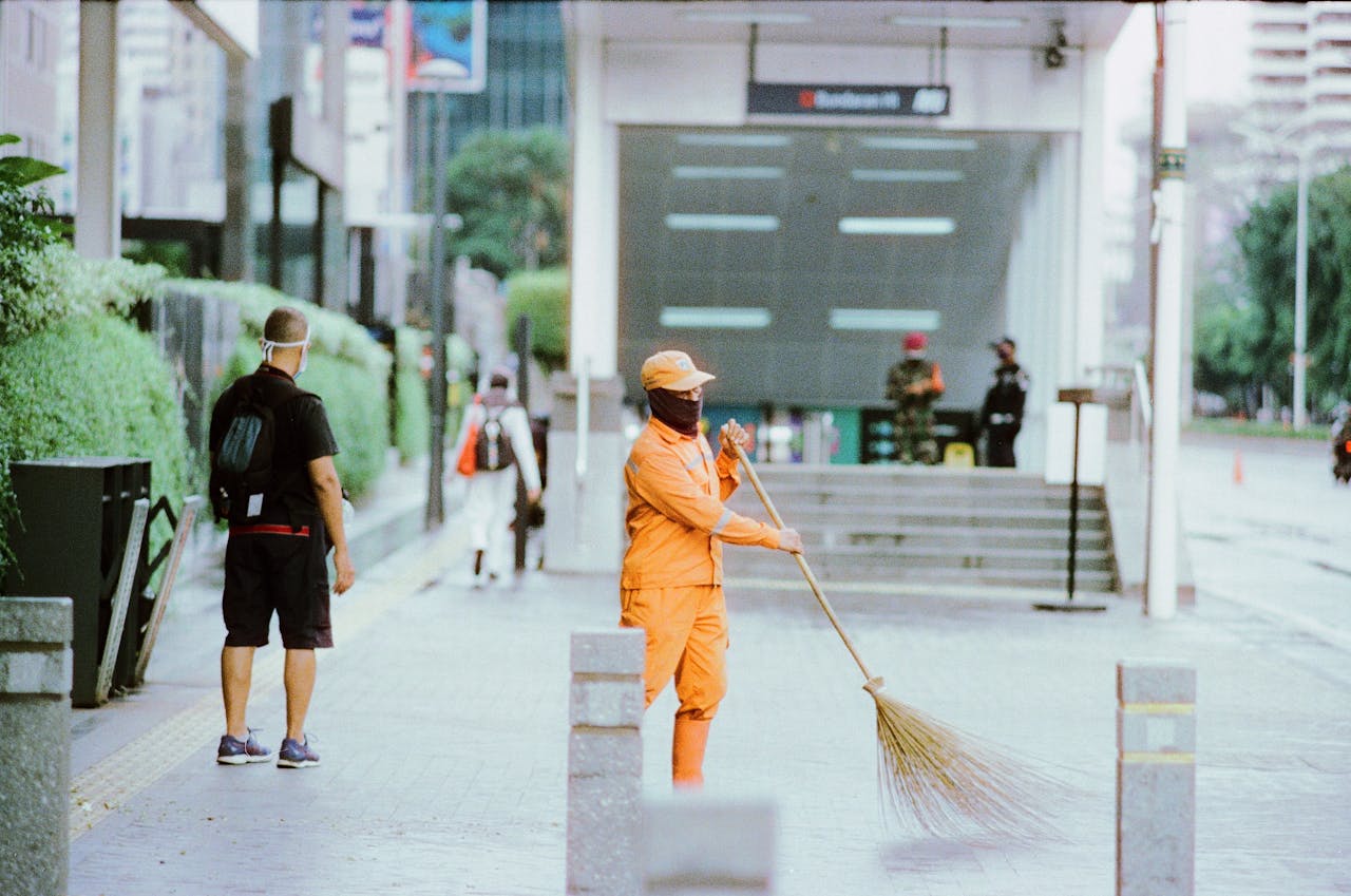 City street cleaner sweeping pavement in bright orange uniform, showcasing urban public service.
